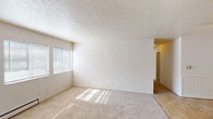This single-floor unit offers a straightforward, functional layout with a neutral color palette of white walls and beige tones throughout. The living area is generously sized, featuring wall-to-wall carpet and a textured ceiling. Natural light filters in through horizontal-blind-covered windows, casting bright patterns across the floor. A wall-mounted air conditioning unit and baseboard heaters provide climate control throughout the space.

The kitchen is efficiently arranged in an L-shaped configuration, equipped with white cabinetry, granite-look countertops, a coil-burner range with an overhead vent hood, and a sink. Light tile flooring extends through the kitchen and entry areas, creating a practical transition from the carpeted rooms.

The bedrooms are carpeted and well-lit, each featuring windows with horizontal blinds and baseboard heating. One bedroom benefits from dual windows, allowing for enhanced natural light.

Two bathrooms serve the unit. One features a vanity with white cabinetry, a toilet, and mosaic tile flooring with baseboard heat. The second includes a wood-toned vanity, a tub-shower combination, a large mirror, and matching mosaic tile flooring. Both are finished in neutral tones, maintaining the unit's consistent, clean aesthetic.