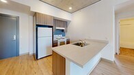 Located at 2045 SW River Parkway in Portland, Oregon, this two-bedroom, one-bathroom unit offers a thoughtfully designed layout with distinctive industrial-modern character. The open-concept kitchen anchors the living area and features a large peninsula with a built-in sink, medium-toned wood cabinetry, a electric range, and a full-size refrigerator. Light hardwood flooring flows throughout the main living and kitchen areas, complementing the exposed concrete ceiling—a standout architectural detail that lends an urban, loft-like aesthetic to the space.

Both bedrooms are carpeted and equipped with ceiling fans. The primary bedroom offers a comfortable footprint with closet access and connects conveniently to the hallway. The second bedroom benefits from multiple large windows that invite natural light and frame outdoor views of the surrounding Portland landscape. Each bedroom features the same exposed concrete ceiling treatment, maintaining a cohesive design language throughout.

The bathroom is well-appointed with warm earth-toned tile flooring, a full soaking tub and shower combination, a wood-paneled vanity with a white countertop, and a large mirror. A hallway connects the rooms efficiently, completing this compact yet functional single-floor residence.