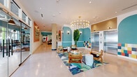 Located at 3533 NW 15th Ave in Miami, FL, this generously sized single-floor amenity space offers a thoughtfully designed environment that blends bold aesthetics with practical functionality. The entrance lobby immediately sets the tone with its eye-catching, resort-inspired interior: teal-painted arched alcoves, terracotta accent walls, polished concrete-style flooring, and a striking circular brass chandelier overhead. Tall tropical plants and vibrant botanical-print area rugs reinforce the lively Miami atmosphere, while elevator access and a colorful mosaic tile feature wall add architectural interest near the main corridor.

Adjacent to the lobby, a glass-enclosed leasing and co-working lounge provides a semi-private workspace with modern furniture, including a plush olive-green velvet sofa and sleek gold accent tables. A built-in bar-height counter with pink arched mirrors and wainscoting serves as a stylish communal workspace or gathering spot.

The fitness center is a standout feature, boasting soaring ceilings, teal walls, and floor-to-ceiling windows that flood the room with natural light and outdoor views. It is outfitted with an extensive range of equipment, including TRX suspension systems, free weights, punching bags, medicine balls, resistance gear, and cardio machines — all set on light hardwood-style flooring beneath industrial pendant lighting.