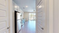 Located at 101 Main St in Little Elm, TX, this single-floor unit offers a thoughtfully designed layout that maximizes functionality within a compact footprint. Light wood-style flooring runs throughout, lending a clean, cohesive look to the entire space.

The open living area is bright and airy, anchored by a ceiling fan with a light fixture and a large sliding glass door that opens to a private balcony, filling the room with natural light and providing outdoor views of the surrounding area.

The kitchen is well-appointed with white shaker-style cabinetry, granite-look countertops, and stainless steel appliances including a refrigerator, range, and built-in microwave. A compact breakfast bar with a pedestal support offers a convenient casual dining option. The layout flows efficiently, making the most of the available space.

A hallway connects the main living area to the remaining rooms, where built-in open shelving provides additional display or storage space. The bathroom features wood-look tile flooring, a granite-topped vanity with shaker-style cabinetry, and a full tub/shower combo with white subway tile surround. A dedicated closet completes the unit, offering practical storage. The overall aesthetic is modern, clean, and move-in ready.