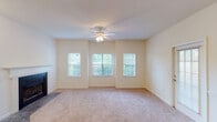 Located at 4450 Platinum Dr in High Point, NC, this single-floor unit offers a well-designed open-concept layout that connects the main living areas seamlessly. The kitchen is a functional centerpiece, featuring taupe shaker-style cabinetry, light speckled countertops, a built-in peninsula with a double sink, and white appliances including a range, over-the-range microwave, and refrigerator. Tile flooring grounds the kitchen, which flows directly into the open living and dining area. The living room is generously proportioned, finished with plush carpeting and a ceiling fan, and benefits from a trio of windows that invite natural light and outdoor views. An additional carpeted room features French doors opening to the exterior, providing flexible use as a bedroom, den, or sitting area. The bathroom is neatly finished with white tile flooring, a tiled tub-surround accented by a teal border, a vanity with under-sink cabinetry, and a lighted mirror. A spacious walk-in closet with multi-level wire shelving offers ample storage. Throughout the unit, neutral walls and light-toned carpeting create a clean, cohesive ambiance.