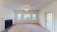 Located at 4450 Platinum Dr in High Point, NC, this single-floor unit offers a well-designed open-concept layout that connects the main living areas seamlessly. The kitchen is a functional centerpiece, featuring taupe shaker-style cabinetry, light speckled countertops, a built-in peninsula with a double sink, and white appliances including a range, over-the-range microwave, and refrigerator. Tile flooring grounds the kitchen, which flows directly into the open living and dining area. The living room is generously proportioned, finished with plush carpeting and a ceiling fan, and benefits from a trio of windows that invite natural light and outdoor views. An additional carpeted room features French doors opening to the exterior, providing flexible use as a bedroom, den, or sitting area. The bathroom is neatly finished with white tile flooring, a tiled tub-surround accented by a teal border, a vanity with under-sink cabinetry, and a lighted mirror. A spacious walk-in closet with multi-level wire shelving offers ample storage. Throughout the unit, neutral walls and light-toned carpeting create a clean, cohesive ambiance.