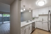 This single-floor residence offers a clean, modern aesthetic throughout, with light-toned hardwood-style flooring and neutral wall finishes creating a bright, cohesive atmosphere. The open-concept layout connects the kitchen and living area seamlessly, promoting an efficient and functional flow.

The kitchen is well-equipped with white shaker-style cabinetry, quartz countertops, a subway tile backsplash, and a full suite of stainless steel appliances including a range, microwave, and dishwasher. A peninsula counter with pendant lighting above serves as a natural divider between the kitchen and the living space, adding both visual interest and utility.

The living area is generously sized, featuring a large sliding glass door that opens to a private patio, allowing abundant natural light to fill the space and providing outdoor views of a fenced exterior area. Vertical blinds offer adjustable privacy.

The bedrooms are well-proportioned, each featuring hardwood-style flooring, textured walls, and windows with blinds that allow natural light. Closet storage is available in at least one bedroom.

The bathroom includes a tub-shower combination with tiled surround, a vanity with a single sink, and a large mirror. Textured ceilings are present throughout, adding architectural character to the overall design.