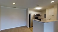 This single-floor residence offers a thoughtfully designed layout across two bedrooms and one bathroom, providing a comfortable and functional living environment. The open-concept design connects the kitchen and living area seamlessly, creating a sense of expansive, flowing space.

The kitchen is a standout feature, equipped with stainless steel appliances including a full-size refrigerator, microwave, and electric range. White cabinetry provides ample storage, while the peninsula-style breakfast bar extends the counter space and offers a casual dining option. Wood-style flooring runs throughout the kitchen, adding warmth and easy maintenance to the space.

The adjoining living area features neutral-toned carpet, creating a cozy, comfortable environment. Soft, neutral wall colors throughout contribute to a clean, welcoming ambiance. Crown molding adds a refined architectural detail, while a textured ceiling and flush-mounted lighting ensure the space is well-lit.

HVAC vents are visibly integrated into the ceiling, ensuring year-round comfort. The overall aesthetic is modern yet understated, with practical finishes that balance style and functionality throughout the residence.