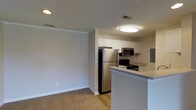This single-floor residence offers a thoughtfully designed layout across two bedrooms and one bathroom, providing a comfortable and functional living environment. The open-concept design connects the kitchen and living area seamlessly, creating a sense of expansive, flowing space.

The kitchen is a standout feature, equipped with stainless steel appliances including a full-size refrigerator, microwave, and electric range. White cabinetry provides ample storage, while the peninsula-style breakfast bar extends the counter space and offers a casual dining option. Wood-style flooring runs throughout the kitchen, adding warmth and easy maintenance to the space.

The adjoining living area features neutral-toned carpet, creating a cozy, comfortable environment. Soft, neutral wall colors throughout contribute to a clean, welcoming ambiance. Crown molding adds a refined architectural detail, while a textured ceiling and flush-mounted lighting ensure the space is well-lit.

HVAC vents are visibly integrated into the ceiling, ensuring year-round comfort. The overall aesthetic is modern yet understated, with practical finishes that balance style and functionality throughout the residence.