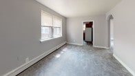 Located at 6000 Tabor Ave in Philadelphia's 19111 zip code, this single-floor unit offers a practical and comfortable layout across multiple rooms. The living area is finished with soft gray carpeting and neutral gray walls, creating a calm, understated atmosphere. Natural light flows in through large windows fitted with blinds, and baseboard heating runs along the walls to ensure year-round comfort. Multiple additional carpeted rooms serve as bedrooms or flexible living spaces, each benefiting from windows that bring in ample daylight and views of the surrounding neighborhood. The kitchen is equipped with rich, warm-toned wood cabinetry, dark laminate countertops, a stainless steel sink positioned beneath a window overlooking greenery, and a gas range. Tile backsplash adds a clean, functional finish to the cooking space. The bathroom features classic vintage-style pink wall tiles accented with deep burgundy border tiles, a wood vanity with sink, a window for natural light, and tile flooring. Throughout the unit, a consistent neutral color palette and well-maintained finishes contribute to a clean, move-in-ready feel. The floorplan, visible in the overhead dollhouse view, presents a compact yet efficiently arranged single-level layout suited for everyday living.