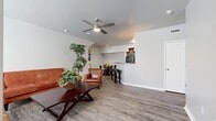 This single-floor residence offers a thoughtfully designed open-concept layout that seamlessly connects the living, dining, and kitchen areas. The spacious living room features durable wood-look flooring, a ceiling fan with light fixture, and recessed lighting, creating a bright and comfortable gathering space. Large windows allow natural light to fill the room, enhancing its warm, neutral color palette.

The kitchen is outfitted with dark cabinetry, granite-style countertops, black appliances, and a convenient breakfast bar with bar seating — ideal for casual dining. Adjacent to the kitchen, a defined dining nook provides an intimate space for sit-down meals, framed by a recessed wall that adds architectural character.

The bedrooms are carpeted for comfort and include ceiling fans, ample natural light from windows, and access to closets. The layout as seen from the dollhouse view indicates multiple bedrooms, each offering a calm and restful atmosphere.

The bathroom is well-appointed with a soaking tub and shower combination, white tile surround, a window for natural light, dark navy cabinetry, granite-top vanity, and wood-look flooring. Additional spaces include a versatile room with wood-look flooring suited for a home office or flex room. Throughout, the neutral tones and clean finishes create a cohesive, move-in-ready aesthetic.