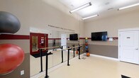 Located at 11289 E Hamilton Crest Blvd in Fishers, Indiana, this single-floor fitness and wellness studio is thoughtfully designed to support movement, exercise, and overall well-being. The space features an open, airy layout with elevated ceilings that create a sense of spaciousness and allow for comfortable, unrestricted movement.

The studio is equipped with freestanding ballet barres running along a full wall of floor-to-ceiling mirrors, making it ideal for balance training, stretching, and a variety of fitness activities. The mirrored wall not only enhances the sense of depth within the room but also allows participants to monitor their form during exercise. A wall-mounted flat-screen television provides a modern touch, suitable for guided workout sessions or instructional content.

A dedicated rack of weighted medicine balls in assorted colors adds a vibrant, functional element to the space, offering a range of options for strength and coordination training. The neutral-toned flooring provides a clean, resilient surface appropriate for physical activity.

Adding to the motivating atmosphere, a bold wall decal reads "Make each day your masterpiece." — a quote attributed to John Wooden — reinforcing the studio's focus on personal growth and daily dedication. The overall design is clean, functional, and welcoming, making it an excellent environment for fitness programming of all kinds.