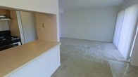 This two-floor residential space offers a straightforward and functional layout designed for comfortable everyday living. The main level showcases an open-concept living area with wall-to-wall carpeting and clean, neutral-toned walls that create a bright and airy atmosphere. A white kitchen peninsula with a light-colored countertop serves as a natural divider between the kitchen and the living space, providing additional prep and seating space while maintaining an open flow between the two areas. The kitchen area features a pass-through nook, adding a practical architectural detail that enhances connectivity between spaces. Electrical fixtures and outlets are positioned throughout for convenient use. The neutral color palette of soft whites and warm beige tones runs consistently across both levels, lending the space a cohesive and understated aesthetic. The open living area offers ample room for furniture arrangement and personalization. With two floors of living space, the layout provides the flexibility to designate areas for different functions, whether for sleeping, working, or leisure. Overall, the space presents a clean, move-in-ready canvas suitable for a variety of living arrangements.