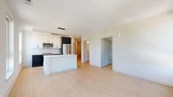 This thoughtfully designed 2-bedroom, 2-bathroom residence offers a clean, contemporary aesthetic throughout its efficiently laid-out single floor. Light wood-toned flooring flows seamlessly across every room, creating a cohesive and airy feel. The open-concept kitchen and living area serves as the heart of the home, featuring a central island with a white quartz countertop, two-tone cabinetry with dark lower cabinets and crisp white uppers, a subway tile backsplash, and stainless steel appliances including a built-in microwave and refrigerator. Large windows along the living area flood the space with natural light and frame views of the surrounding urban landscape and greenery. A well-proportioned hallway connects the living area to the private quarters, with louvered closet doors providing convenient storage access. The primary bedroom offers double closets and two windows with pleasant outdoor views. The second bedroom is equally bright, benefiting from a large corner window. Both bathrooms are finished in white, with wood-look tile flooring, white vanities with ample drawer storage, and clean subway tile surrounds — one featuring a tub-shower combination and the other a glass-enclosed walk-in shower.