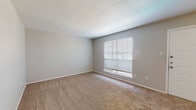 This single-story residence offers a straightforward, functional layout designed to maximize comfort and usability. The entry area welcomes residents through a solid panel door into a generously sized living space finished with neutral-toned carpeting and light gray walls, creating a clean, versatile backdrop. A large window fitted with horizontal blinds allows natural light to fill the room, contributing to a bright and open atmosphere.

The living area transitions seamlessly toward a secondary space equipped with a ceiling fan with integrated lighting, providing both comfort and practicality. Adjacent to this area, a partial wall separates the living space from the kitchen, which features white cabinetry, white appliances, and hard-surface flooring, offering a functional cooking environment.

The bedrooms are carpeted and finished consistently with the rest of the home in neutral tones. Each room includes a ceiling fan with light fixture and windows with blinds for natural light and privacy. The primary bedroom provides access to a dedicated walk-in closet and a connected bathroom, visible through separate doorways. The textured ceilings are present throughout, adding a subtle design detail consistent across the entire home.