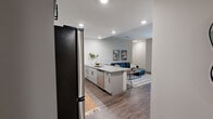 This single-floor residence offers six bedrooms and four bathrooms, thoughtfully designed with a clean, modern aesthetic throughout. The open-concept kitchen and living area serves as the heart of the home, featuring white shaker cabinets with matte black hardware, granite countertops, a subway tile backsplash, and a full suite of stainless steel appliances. A peninsula with seating connects the kitchen to the living space, which is brightened by large windows with views to the outdoors. Wood-look plank flooring runs continuously throughout, lending warmth and visual cohesion to the entire space. Two hallways branch off the main living area, providing efficient access to the six bedrooms — each a comfortably scaled, private retreat with neutral walls and recessed lighting. The four bathrooms are uniformly finished with granite-topped vanities, shaker-style cabinetry, framed mirrors, and tiled tub-shower combinations. The consistent use of granite countertops, matte black fixtures, and a neutral color palette across every room creates a cohesive, contemporary feel. The layout is well-suited for multi-occupant living, balancing shared communal spaces with ample private accommodations.