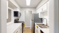 This single-floor residence offers a practical and clean layout designed for comfortable everyday living. The galley-style kitchen is efficiently organized, featuring stainless steel appliances including an electric range, over-the-range microwave, and refrigerator, complemented by white shaker cabinetry, light countertops, and light wood-tone flooring. A dedicated laundry room off the kitchen provides added convenience with a side-by-side washer and dryer setup and overhead shelving.

The living area extends toward a full-width sliding glass door that invites natural light and provides access to an outdoor space. Neutral-toned walls and wood-style flooring carry throughout the common areas, creating a cohesive feel. The bedrooms are carpeted and generously sized, each featuring windows with blinds that allow natural light while maintaining privacy.

Two bathrooms serve the unit, each appointed with white vanity cabinetry, light countertops, large mirrors with overhead lighting, and wood-tone flooring. One bathroom is accessible directly from a bedroom, offering added functionality. Throughout, the unit maintains a neutral, well-maintained aesthetic well-suited for a variety of living arrangements.