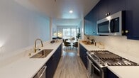 Located at 138 N Beaudry Ave in downtown Los Angeles, this contemporary two-floor residence offers a thoughtfully designed interior with a cohesive modern aesthetic throughout. The open-concept living area is anchored by large windows that frame views of swaying palm trees and a landscaped courtyard with a pool, flooding the space with natural light. Hardwood-style flooring flows seamlessly across both levels, complementing the clean white walls and bold navy accents.

The galley-style kitchen is a standout feature, outfitted with deep navy cabinetry, gold hardware, white quartz countertops, a gold-toned faucet, and stainless steel appliances including a gas range. It opens directly to a dining area and living room, creating an ideal layout for entertaining. A compact half bath on one level provides added convenience.

The bedroom is a serene retreat, highlighted by a dramatic navy accent wall, a closet, and a sliding glass door leading to an outdoor area with views of mature palms. A well-appointed bathroom features a navy vanity with gold hardware, wood-look flooring, and angled ceiling details. Additional storage is provided by a dedicated closet with built-in shelving. The space presents a refined, design-forward living environment in the heart of Los Angeles.