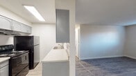 This single-floor unit offers a clean, functional layout with a thoughtful blend of materials and finishes throughout. The open living area is highlighted by light wood-style laminate flooring, neutral walls, and a textured ceiling, creating a bright and welcoming atmosphere. A dedicated entry closet provides convenient storage just inside the front door.

The galley-style kitchen is well-appointed with gray cabinetry, light countertops, a stainless steel sink, and a classic white subway tile backsplash. Black appliances, including a refrigerator and electric range, complete the space, which is illuminated by overhead lighting. A peninsula counter with an upper cabinet separates the kitchen from the living area, adding a subtle sense of division while maintaining an open feel.

The bedroom features plush carpeting, a ceiling fan with integrated lighting, a baseboard heater, and a window that invites natural light. The textured ceiling carries through from the main living areas, providing a consistent aesthetic.

The bathroom is finished with wood-style flooring, a gray vanity with a light countertop and single sink, a toilet, and a tiled tub/shower combination. Chrome fixtures and clean white tile walls contribute to a fresh, well-maintained appearance throughout the unit.