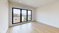 Located on the fifth floor at 1525 N American St in Philadelphia's vibrant Northern Liberties neighborhood, this contemporary unit offers a thoughtfully designed open-concept layout. Light hardwood flooring runs throughout, lending warmth and continuity to the space.

The kitchen is a standout feature, equipped with stainless steel appliances including a full-size refrigerator and electric range, sleek flat-front cabinetry in a neutral tone, and a large island with a built-in sink and quartz-style countertop. Stylish pendant lights hang above the island, adding a modern accent. Recessed lighting throughout ensures a bright, clean ambiance.

The open living area flows seamlessly from the kitchen and is bathed in natural light courtesy of expansive floor-to-ceiling windows framed in bold black. These large windows offer elevated views of the surrounding Philadelphia streetscape, bringing the energy of the city indoors while maintaining a sense of openness. A separate bedroom space features its own generously sized window, continuing the theme of natural light and urban views.

The overall design aesthetic is clean and modern — white walls, minimalist finishes, and an efficient use of space create a polished, contemporary feel well-suited to urban living in one of Philadelphia's most dynamic neighborhoods.