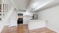 Located at 1400 Fuller Ct in Lancaster, Ohio, this two-story home offers a thoughtfully laid-out floor plan across two levels. The main floor features a combined kitchen and living area finished with warm hardwood-style flooring and exposed beam detailing on the ceiling. The kitchen stands out with crisp white shaker cabinetry, marble-look countertops, a peninsula with additional counter seating, and a full suite of stainless steel appliances including a range, microwave, dishwasher, and refrigerator. Track lighting overhead enhances the bright, open feel of the space. A white-railed staircase leads to the upper level, where both bedrooms are finished with plush carpeting, soft gray walls, and ceiling fans with integrated lighting. Each bedroom benefits from natural light through blinded windows. The primary bedroom offers generous closet storage, including a built-in double closet and an open shelving unit. The full bathroom is clean and functional, featuring a soaker tub and shower combination with a curved curtain rod and light wood-style flooring. A hallway connects the upstairs rooms efficiently. Throughout the home, a consistent neutral color palette and modern fixtures create a cohesive, move-in-ready aesthetic.