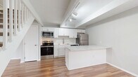 Located at 1400 Fuller Ct in Lancaster, Ohio, this two-story home offers a thoughtfully laid-out floor plan across two levels. The main floor features a combined kitchen and living area finished with warm hardwood-style flooring and exposed beam detailing on the ceiling. The kitchen stands out with crisp white shaker cabinetry, marble-look countertops, a peninsula with additional counter seating, and a full suite of stainless steel appliances including a range, microwave, dishwasher, and refrigerator. Track lighting overhead enhances the bright, open feel of the space. A white-railed staircase leads to the upper level, where both bedrooms are finished with plush carpeting, soft gray walls, and ceiling fans with integrated lighting. Each bedroom benefits from natural light through blinded windows. The primary bedroom offers generous closet storage, including a built-in double closet and an open shelving unit. The full bathroom is clean and functional, featuring a soaker tub and shower combination with a curved curtain rod and light wood-style flooring. A hallway connects the upstairs rooms efficiently. Throughout the home, a consistent neutral color palette and modern fixtures create a cohesive, move-in-ready aesthetic.
