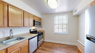 Located at 3100 Southgate Drive in Alexandria, Virginia, this one-bedroom, one-bathroom residence offers a well-organized, single-floor layout designed for comfortable everyday living. The expansive living room is finished with soft, neutral-toned carpeting and features a sliding glass door that fills the space with natural light while providing access to the outdoors. The open feel of the room is enhanced by clean white walls and a straightforward flow into the rest of the home. The kitchen is a functional highlight of the unit, boasting warm honey-toned cabinetry, stainless steel appliances including a gas range, built-in microwave, and dishwasher, along with light countertops and durable hardwood-style flooring. A bright window overlooking the outdoors adds a welcoming touch to the cooking area. The bedroom offers a comfortable footprint with plush carpeting, neutral walls, and ample closet space — the home includes three closets in total, one of which is a generously sized walk-in with built-in shelving and hanging rods. The bathroom features a full tub and shower combination with clean white tile surround and chrome fixtures. A connecting hallway ties all areas together seamlessly, contributing to the home's efficient and practical layout.