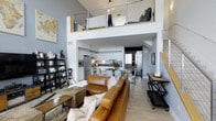 Located at 6800 Embarcadero Lane in Carlsbad, this furnished multi-story space offers a striking architectural layout across three floors. The main living area commands attention with soaring double-height ceilings, light wood flooring, and an open-concept design that seamlessly connects the living room, dining area, and kitchen. A contemporary staircase with cable railings and wood accents leads to an upper loft level, adding visual drama to the space.

The kitchen is well-appointed with sleek white cabinetry, stainless steel appliances including a professional-grade range, a mosaic tile backsplash, and dark countertops. A solid wood dining table anchors the adjoining dining area, completing the open-plan layout.

One bedroom features a sophisticated, moody aesthetic with textured charcoal wall coverings, a ceiling fan, framed artwork, and a frosted glass sliding barn door. The upper-level bedroom offers a cozy loft ambiance with angled ceilings, Edison bulb pendant lighting, and open railing overlooking the living space below.

The bathrooms are thoughtfully designed — one features floor-to-ceiling white tile, a glass-enclosed combination tub and shower, and clean minimalist finishes, while a second bath offers dark cabinetry, a large mirror, and a walk-in shower. This space delivers a cohesive blend of modern industrial and contemporary design throughout.