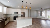 This well-appointed 3-floor home showcases a cohesive modern design throughout. The main living level centers on an open-concept kitchen and living area finished with durable wood-look flooring. The kitchen is a standout feature, equipped with stainless steel appliances including a French door refrigerator, electric range, microwave, and dishwasher. White and taupe shaker-style cabinetry pairs with a mosaic tile backsplash, while a large central island with a quartz countertop provides generous workspace and seating. Three geometric gold pendant lights hang above the island, adding a contemporary accent. A built-in wine rack and open shelving add functional character. The adjoining living area is bright and open, featuring a ceiling fan and natural light from nearby windows. Bedrooms feature plush carpeting, ceiling fans, and natural light. Bathrooms are finished with tile flooring, including a secondary bath with a tub-shower combo and white subway tile surround, and a primary bath with a double vanity, quartz countertops, and a glass-enclosed shower. The ground level includes an attached garage with a sloped ceiling, offering practical storage or parking.