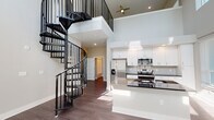 This contemporary two-story residence in Jacksonville, FL (32207) offers a thoughtfully designed layout with modern finishes throughout. The centerpiece of the main level is a striking black spiral staircase that anchors the open-concept living and kitchen area, which soars with dramatic double-height ceilings and is bathed in natural light from an expansive bank of windows. The kitchen is well-appointed with white shaker cabinetry, granite countertops, stainless steel appliances including a French door refrigerator, and a central island that provides ample workspace and storage. Dark wood-style flooring runs throughout the main living areas, complementing the clean, neutral color palette. The upper level features a loft-style overlook with a ceiling fan and multiple windows framing lush green views of the surrounding landscape. Bedrooms are generously sized and finished with plush carpet and ample closet space, including walk-in closets with built-in shelving. The primary bathroom offers a double vanity with granite countertops, a walk-in glass shower, and dark hardwood-style flooring, while a secondary bathroom includes a full tub-shower combination and matching granite finishes. Hallways are bright and spacious, reinforcing the open, airy character of the home.