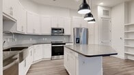 This thoughtfully designed 2-bedroom, 2-bathroom single-story residence offers a clean, contemporary aesthetic with high-quality finishes throughout. The open-concept kitchen and living area serves as the heart of the home, featuring crisp white shaker-style cabinetry extending to the ceiling, a geometric hexagonal tile backsplash, dark contrasting countertops, and a central kitchen island illuminated by a trio of modern pendant lights. Stainless steel appliances, including a French door refrigerator with ice maker and a range with over-the-range microwave, complete the well-appointed kitchen. The living area extends seamlessly from the kitchen and includes a built-in shelving unit, offering both function and character. Wood-look plank flooring flows consistently throughout the entire residence, adding warmth to the otherwise bright, neutral palette. The generously sized primary bedroom provides ample space and includes access to a well-sized closet with full shelving and hanging rods. The second bedroom is served by natural light from a window with blinds. The bathrooms are finished with large-format tile surrounds over soaking tubs. Two hallways and two closets round out the practical layout of this polished, move-in-ready residence.