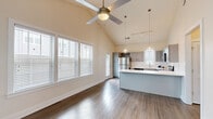 Located at 406 Ledbury Rd in Wilmington, NC, this thoughtfully designed one-bedroom, two-bathroom home maximizes every inch of its compact footprint. The open-concept living and kitchen area immediately impresses with dramatic vaulted ceilings, a ceiling fan, and an abundance of natural light streaming through multiple windows dressed with classic blinds. Rich hardwood-style flooring runs throughout, providing a cohesive and polished look. The kitchen is a standout feature, showcasing grey shaker-style cabinetry, white quartz countertops, a subway tile backsplash, and a full suite of stainless steel appliances including a refrigerator, microwave, range, and dishwasher. A peninsula island with pendant lighting adds both functionality and style, creating an ideal space for casual dining or meal prep. The bedroom offers a calm, neutral retreat with hardwood-style flooring, a window with natural light, and direct access to a closet. The bathrooms are clean and modern, one featuring a glass-enclosed shower and tub combo with a grey vanity and mirror. The exterior reveals a charming grey-sided structure with a pitched roof, a concrete patio, and a fenced yard with lush artificial turf — a low-maintenance outdoor space perfect for relaxing or entertaining.