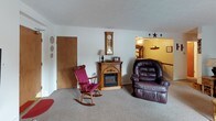This single-floor, two-bedroom home offers a comfortable and inviting layout with a warm, homey character throughout. The spacious living room serves as the heart of the home, featuring a wood-trimmed electric fireplace with a decorative mantel, carpeted flooring, and an open passage to an adjacent sitting or family area. The living spaces are furnished with plush seating and accented with classic country-style décor, creating a cozy and relaxed atmosphere.

The galley-style kitchen is efficiently laid out with dark wood cabinetry, white appliances including a range and refrigerator, a double sink, and light tile flooring. Ample upper cabinet storage and a textured ceiling complete the functional design.

Both bedrooms are carpeted and feature warm tan-toned walls, natural light from curtained windows, and generous space for furnishings. One bedroom offers a traditional wood-framed bed with a classic dresser, while the second bedroom features a lighter, painted furniture set in a soft, relaxed style.

The full bathroom includes a tiled tub-shower combination, a vanity with storage, tile flooring, and decorative border detailing near the ceiling, offering a clean and well-appointed space.

Overall, this home presents a welcoming, traditional aesthetic with practical amenities throughout.