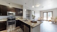 This single-story residence offers a thoughtfully designed open-concept layout that seamlessly connects the kitchen, dining, and living areas. The kitchen serves as the centerpiece, showcasing granite countertops, dark espresso cabinetry with brushed nickel hardware, and a tile mosaic backsplash. A peninsula with a double stainless steel sink and pendant lighting above provides additional prep space and a natural gathering point. Stainless steel appliances, including a range, microwave, and refrigerator, complete the functional setup. Built-in open shelving between the kitchen and living area adds convenient display and storage space.

The living area features wood-style flooring and a sliding glass door that invites natural light and outdoor views. The bedrooms are carpeted and equipped with ceiling fans and windows that bring in additional natural light. A spacious walk-in closet with wire shelving and multiple hanging levels offers generous storage capacity.

The bathrooms are finished with tile flooring, granite-topped dark vanities, and well-lit mirrors. The primary bath features a double-sink vanity, a soaking tub, and direct access to the bedroom. A secondary bath offers similar finishes with practical storage cabinetry.