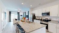Located at 2108 Silty Soil Ct in Leland, NC, this two-story home offers a well-designed layout across two floors. The main level is anchored by a bright, open-concept kitchen and living area. The kitchen is outfitted with white shaker cabinetry, granite countertops, stainless steel appliances, and a large island with bar seating — ideal for entertaining. Light wood-look flooring flows seamlessly into the living room, which features large windows dressed with bold striped curtains, flooding the space with natural light. A welcoming entryway hallway with recessed lighting leads into the heart of the home.

Upstairs, the more expansive floor houses both bedrooms, three bathrooms, a dedicated office, and multiple closets. The spacious primary bedroom is filled with natural light from multiple windows and includes a ceiling fan. The en-suite bathroom features granite countertops, white cabinetry, and direct access to a walk-in closet. The second bedroom is equally bright and well-appointed. The dedicated office provides a quiet, versatile retreat. Throughout the home, light-toned luxury vinyl plank flooring, recessed lighting, and a clean, neutral color palette create a cohesive and modern aesthetic.