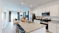 Located at 2108 Silty Soil Ct in Leland, NC, this two-story home offers a well-designed layout across two floors. The main level is anchored by a bright, open-concept kitchen and living area. The kitchen is outfitted with white shaker cabinetry, granite countertops, stainless steel appliances, and a large island with bar seating — ideal for entertaining. Light wood-look flooring flows seamlessly into the living room, which features large windows dressed with bold striped curtains, flooding the space with natural light. A welcoming entryway hallway with recessed lighting leads into the heart of the home.

Upstairs, the more expansive floor houses both bedrooms, three bathrooms, a dedicated office, and multiple closets. The spacious primary bedroom is filled with natural light from multiple windows and includes a ceiling fan. The en-suite bathroom features granite countertops, white cabinetry, and direct access to a walk-in closet. The second bedroom is equally bright and well-appointed. The dedicated office provides a quiet, versatile retreat. Throughout the home, light-toned luxury vinyl plank flooring, recessed lighting, and a clean, neutral color palette create a cohesive and modern aesthetic.