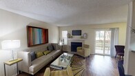 Located in the Bent Tree Forest area of Dallas, Texas, this single-story residence offers a well-organized layout designed for comfortable everyday living. The living room serves as the heart of the home, featuring rich hardwood flooring, a wood-burning fireplace with a white surround and mounted flat-screen TV above, and a sliding glass door that opens to a private outdoor balcony. Natural light filters in through multiple windows, creating a bright and welcoming ambiance. Adjacent to the living area is an intimate dining space, also with balcony access and hardwood floors, ideal for casual meals. The galley-style kitchen is outfitted with warm wood cabinetry, granite-look countertops, a double sink, and black appliances, providing efficient functionality. A dedicated bedroom offers plush carpeting, a ceiling fan, and natural light through blinds. A flexible room serves as a home office or secondary bedroom, complete with carpet, a ceiling fan, and ample wall space. The bathroom features a tiled tub-shower combination, wood-look flooring, and granite-look vanity countertops. An in-unit laundry area with a full-size washer and dryer adds everyday convenience. Throughout, textured ceilings and neutral tones create a cohesive, functional living environment.