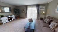 This single-floor residence offers a thoughtfully designed layout that balances comfort and functionality across its key living spaces. The living room serves as the heart of the home, featuring plush wall-to-wall carpeting, warm taupe-toned walls, and a large sliding glass door framed by vertical blinds and draped curtains that flood the room with natural light and provide direct access to an outdoor balcony with open views. A wall-mounted air conditioning unit and baseboard heating ensure year-round comfort.

The kitchen is equipped with ample white cabinetry, dark granite-style countertops, a double sink, and white appliances including a range and dishwasher, all set atop rich hardwood-style flooring that extends into the bathroom. The bathroom features a vanity with a large mirror, a tub-shower combination, and bright overhead lighting.

The two bedrooms are carpeted and finished in the same neutral palette, each offering a tranquil atmosphere with windows that bring in natural light and outdoor views. Closet access is conveniently positioned in each room. The overall design maintains a consistent, understated aesthetic throughout, creating a cohesive and comfortable living environment.