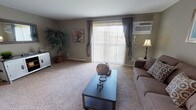 This single-floor residence offers a thoughtfully designed layout that balances comfort and functionality across its key living spaces. The living room serves as the heart of the home, featuring plush wall-to-wall carpeting, warm taupe-toned walls, and a large sliding glass door framed by vertical blinds and draped curtains that flood the room with natural light and provide direct access to an outdoor balcony with open views. A wall-mounted air conditioning unit and baseboard heating ensure year-round comfort.

The kitchen is equipped with ample white cabinetry, dark granite-style countertops, a double sink, and white appliances including a range and dishwasher, all set atop rich hardwood-style flooring that extends into the bathroom. The bathroom features a vanity with a large mirror, a tub-shower combination, and bright overhead lighting.

The two bedrooms are carpeted and finished in the same neutral palette, each offering a tranquil atmosphere with windows that bring in natural light and outdoor views. Closet access is conveniently positioned in each room. The overall design maintains a consistent, understated aesthetic throughout, creating a cohesive and comfortable living environment.