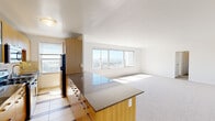 This single-floor residence offers a clean, modern aesthetic with a thoughtfully designed open layout. The spacious living area is anchored by large picture windows that frame sweeping panoramic views of the surrounding cityscape and rolling hills, allowing abundant natural light to pour across the neutral-toned carpeted floors. The open-concept kitchen flows seamlessly into the living space and features warm bamboo-style cabinetry, polished granite countertops, a stainless steel sink, subway tile backsplash, and stainless steel appliances including a refrigerator, gas range, and microwave. A peninsula-style breakfast bar provides additional workspace and casual dining. The bedrooms are bright and carpeted, each benefiting from generous window exposure with scenic outdoor views, and include built-in closets with double hanging rods for organized storage. The bathroom is finished with full subway tile walls, a pedestal sink, a mirrored medicine cabinet with a bamboo-accented wall-mounted storage unit, and a shower-tub combination. Throughout the residence, the consistent use of light-toned finishes, natural wood accents, and an abundance of natural light creates a calm and inviting atmosphere well-suited for comfortable everyday living.