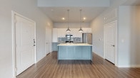 This single-floor, two-bedroom, two-bathroom residence offers a well-designed layout with contemporary finishes throughout. The open-concept kitchen serves as the heart of the space, showcasing a central island with a light countertop and soft blue-gray cabinetry below, complemented by white upper cabinets and a mosaic tile backsplash in muted blues and grays. Stainless steel appliances, including a refrigerator, range, and built-in microwave, add a polished look, while pendant lights with metallic shades hang above the island for focused task lighting. Wood-look flooring runs throughout the main living and kitchen areas, lending warmth and cohesion.

The bedrooms feature plush carpeting, neutral gray walls, and natural light from windows with blinds, creating calm, restful environments. Both bathrooms maintain a clean, modern aesthetic with light tile flooring, tub-shower combinations framed by white subway tile, and vanities topped with dark countertops and undermount sinks. One bathroom features white cabinetry, while the other offers a more streamlined floating vanity with a large mirror. Overall, the space presents a cohesive, modern design with a neutral palette and quality finishes.