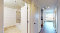 Located at Reston Station Boulevard in Reston, Virginia, this single-floor unit offers a clean, modern aesthetic throughout. The open-concept layout connects the living area to a well-designed kitchen, creating a cohesive and functional living space. The kitchen features white flat-front cabinetry with sleek bar-pull hardware, dark stone countertops, and stainless steel appliances, all finished with hardwood-style flooring that carries through the main living areas.

The spacious living area is characterized by bright white walls, warm wood-tone flooring, and an open passage to the kitchen with a peninsula-style counter. Natural light flows generously through multiple large windows fitted with horizontal blinds, offering views of the surrounding Reston area.

The primary bathroom includes a wide vanity with white cabinetry, dark stone countertops, an undermount sink, and large-format light tile flooring. A second full bathroom features a tub-shower combination with tile surround and a curved shower rod. A hallway connects the living spaces to the private areas, maintaining a logical and efficient flow throughout the unit.