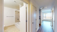 Located at Reston Station Boulevard in Reston, Virginia, this single-floor unit offers a clean, modern aesthetic throughout. The open-concept layout connects the living area to a well-designed kitchen, creating a cohesive and functional living space. The kitchen features white flat-front cabinetry with sleek bar-pull hardware, dark stone countertops, and stainless steel appliances, all finished with hardwood-style flooring that carries through the main living areas.

The spacious living area is characterized by bright white walls, warm wood-tone flooring, and an open passage to the kitchen with a peninsula-style counter. Natural light flows generously through multiple large windows fitted with horizontal blinds, offering views of the surrounding Reston area.

The primary bathroom includes a wide vanity with white cabinetry, dark stone countertops, an undermount sink, and large-format light tile flooring. A second full bathroom features a tub-shower combination with tile surround and a curved shower rod. A hallway connects the living spaces to the private areas, maintaining a logical and efficient flow throughout the unit.