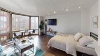 Located at 1130 N Dearborn Street in Chicago's prestigious Gold Coast neighborhood, this single-floor residence offers a thoughtfully designed open-concept layout filled with natural light and contemporary finishes throughout.

The main living area serves as the heart of the space, showcasing rich hardwood flooring, track lighting, and expansive floor-to-ceiling windows that frame impressive views of the Chicago skyline. The open plan seamlessly accommodates both a sleeping area and a living and dining zone, creating a versatile and airy environment.

The kitchen is efficiently designed with light wood cabinetry extending to the ceiling for ample storage, clean white countertops, a white tile backsplash, and stainless steel appliances including a full range. The layout maximizes functionality while maintaining a cohesive, modern aesthetic.

The bathroom features neutral stone-look tile flooring, a vanity with warm wood cabinetry, a tub-shower combination with tile surround, and soft ambient lighting, creating a calm and practical retreat.

Throughout the residence, a consistent palette of warm neutrals and natural wood tones establishes a welcoming ambiance. The abundance of natural light, paired with sweeping urban views, makes this Gold Coast location a compelling urban living option.