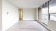 This 2-bedroom, 1-bathroom single-floor residence offers a clean, modern aesthetic throughout, characterized by a neutral color palette, light wood-look flooring, and crisp white trim that unify each room seamlessly. The entry hallway welcomes residents with a bright, open feel, leading naturally into the rest of the home. The living room is a generous, light-filled space anchored by a large sliding glass door that invites natural light and provides access to an outdoor area, with views of the surrounding brick exterior architecture. The galley-style kitchen is thoughtfully designed with white shaker cabinetry, brushed nickel hardware, light quartz countertops, a stainless steel sink, and a full suite of stainless steel appliances including a refrigerator, electric range, and over-the-range microwave — all finished with a classic white tile backsplash. The primary bedroom offers a comfortable footprint with a full-width sliding panel closet for ample storage. The second bedroom similarly features a sliding panel closet and easy hallway access. The bathroom is finished with a full-size soaking tub and shower, surrounded by clean white rectangular wall tiles and chrome fixtures. Three hallways connect the spaces efficiently, completing this well-organized and move-in-ready home.