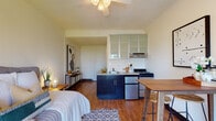 Located at 1455 SW Broadway in the heart of Portland, Oregon, this studio unit offers a well-designed, open-concept layout that maximizes every square foot of available space. Warm hardwood flooring flows throughout the main living area, creating a cohesive and inviting atmosphere. The sleeping area is positioned near a large window that frames views of the surrounding Portland cityscape, with a ceiling fan overhead providing both light and air circulation.

The open kitchenette is thoughtfully arranged along one wall, featuring dark lower cabinetry, frosted-glass upper cabinets, a coil-top range, a stainless steel compact refrigerator, and a single-basin sink with stone-toned countertops. A dedicated dining area accommodates a high-top table and barstools, making efficient use of the available floor space.

A separate full bathroom includes a combined tub and shower, a wall-mounted sink, and tile flooring, maintaining a clean and functional aesthetic. Textured ceilings are present throughout the unit, adding subtle architectural character. Natural light is a consistent feature, with windows on multiple sides drawing in daylight and offering open urban views. The overall ambiance is compact yet comfortable, well-suited for urban living in one of Portland's most walkable and centrally located neighborhoods.