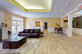 Located at 203 Pinewoods Crescent in Middle Island, NY, this single-story community clubhouse offers a diverse range of amenities designed for comfort, recreation, and socializing. The welcoming entrance foyer features warm herringbone-patterned tile flooring, decorative columns, wainscoting, and a pendant light fixture, setting an inviting tone throughout.

The main social lounge is a bright, open gathering space with light hardwood floors, a tray ceiling with warm yellow accents, crown molding, recessed lighting, and a grand piano — a true centerpiece for community events. Adjacent is a cozy seating area with rich leather sofas, a classic fireplace with white surround, wall-mounted TV, and French doors leading to an outdoor patio.

A billiards room connects seamlessly to the lounge, while a casual dining area with patterned carpeting and wall-mounted TV provides a relaxed setting for meals or gatherings. The compact kitchenette is fully equipped with cabinetry, a refrigerator, dishwasher, microwave, and coffee station.

The fitness center is well-equipped with multi-use cable machines, treadmills, a heavy bag, and free weights, all set against yellow walls and ample natural light. A library and computer room, finished with soft blue-gray walls and plush carpeting, offers comfortable seating, bookshelves, and workstations for quiet use.