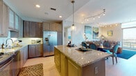 This thoughtfully designed single-floor residence offers a seamless blend of modern functionality and refined aesthetics. The open-concept kitchen is a standout feature, showcasing rich dark-stained cabinetry, granite countertops, a full suite of stainless steel appliances, and a central island with bar seating — ideal for both meal preparation and casual dining. Recessed lighting and pendant fixtures illuminate the space with a warm, inviting glow. The kitchen flows naturally into the dining and living areas, where track lighting highlights vibrant artwork and a generously sized sectional sofa anchors a stylish, comfortable gathering space. The bedrooms are carpeted and serene, each benefiting from floor-to-ceiling windows that frame sweeping city skyline views, flooding the rooms with natural light. The primary bathroom offers a long vanity with granite countertops, dual sinks, large-format tile flooring, and direct access to a walk-in closet with built-in shelving. A second full bathroom also provides a double-sink vanity with dark granite and a dedicated walk-in closet. Additional highlights include an in-unit laundry closet with a full-size washer and dryer, and light hardwood flooring throughout the main living areas, creating a cohesive and polished interior.