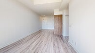 This thoughtfully designed 2-bedroom, 1-bathroom unit offers a clean, modern aesthetic throughout its well-appointed single floor. The open-concept living and kitchen area is anchored by a sleek galley-style kitchen featuring warm wood cabinetry, white countertops, stainless steel appliances including a range, microwave, and dishwasher, and track lighting overhead. Light wood-tone flooring runs seamlessly through the living area, which opens onto a balcony through large floor-to-ceiling windows that flood the space with natural light and offer expansive outdoor views.

The generously sized primary bedroom is a standout feature, boasting oversized windows with a transom detail that frame sweeping views and bathe the room in sunlight. Both bedrooms are finished with light hardwood-style flooring and include built-in sliding closets with clean white panel doors, providing ample storage.

The full bathroom is finished with large-format beige floor tiles, warm taupe subway-tiled walls surrounding a soaking tub and shower combo, and a wood-accented vanity with a white countertop, lending a contemporary yet inviting feel. Throughout the unit, bright white walls, clean lines, and consistent flooring create a cohesive and modern living environment.