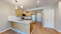 Located at 1530 Empire Blvd in Webster, NY, this well-appointed 2-bedroom, 2-bathroom residence offers a thoughtfully designed single-level layout with modern finishes throughout. Light-toned hardwood-style flooring flows through the open-concept living, dining, and kitchen areas, creating a cohesive and airy feel. The kitchen is a standout feature, showcasing warm maple cabinetry, white subway tile backsplash, a quartz peninsula with pendant lighting overhead, and a full suite of stainless steel appliances including a refrigerator, range, microwave, and dishwasher. The combined living and dining area is bright and open, receiving natural light through large windows that frame views of surrounding greenery. Both bedrooms are generously sized, with large windows, neutral carpet, and ample natural light. The primary bedroom offers a comfortable retreat with its own well-proportioned layout. The bathrooms are elegantly finished, featuring marble-look tile surrounds, sliding glass shower enclosures, white quartz vanity tops, and dark-toned cabinetry. A dedicated laundry area with a stacked washer and dryer adds everyday convenience. Recessed lighting and clean neutral wall tones complete the polished, move-in-ready aesthetic throughout this residence.