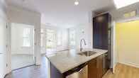 This efficiently designed one-bedroom, one-bathroom unit offers a thoughtful layout across a single floor, making excellent use of its compact footprint. The kitchen serves as a focal point, showcasing a curved granite countertop island with an undermount stainless steel sink, rich dark cabinetry, a tile backsplash, and a full suite of stainless steel appliances including a refrigerator, range, and built-in microwave. A skylight above the kitchen adds a bright, airy quality to the space. The open-plan living area flows naturally from the kitchen, bathed in natural light from multiple windows with views of the surrounding greenery. The bedroom is a serene retreat, featuring plush wall-to-wall carpet, a ceiling fan, and dual windows that frame pleasant outdoor views. A built-in granite-topped desk with dark cabinetry provides a functional workspace within the unit. The bathroom is finished with large-format tile flooring, a soaking tub, and a modern heated towel rail. A dedicated laundry room with wire shelving adds everyday convenience. The unit's clean, neutral palette and consistent use of dark wood tones and granite surfaces create a cohesive, modern aesthetic throughout.