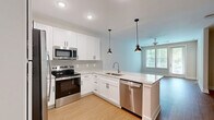 Located at 6050 Harbour Glenn Dr in Midlothian, Virginia, this well-appointed one-bedroom, one-bathroom residence offers a thoughtfully designed single-level layout filled with natural light and modern finishes. The open-concept kitchen and living area serves as the heart of the home, featuring crisp white shaker cabinetry, light granite countertops, a neutral tile backsplash, and a full suite of stainless steel appliances including a French door refrigerator, electric range, built-in microwave, and dishwasher. Stylish pendant lighting anchors the kitchen peninsula, which flows seamlessly into the living area. The living room is bright and airy, with large windows and a glass-paneled door that frame lush green outdoor views and allow abundant natural light to fill the space. A ceiling fan adds comfort and functionality. Warm wood-look flooring runs throughout, providing a cohesive and clean aesthetic. The bedroom is generously proportioned, featuring a triple window with serene tree views, a ceiling fan, and access to a dedicated closet with built-in wire shelving for organized storage. The bathroom offers a wide vanity with granite countertops, white cabinetry, a large mirror, and elegant light fixtures, maintaining the home's consistent, polished design language.