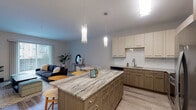 Located along Ferry Road in Warrenville, Illinois, this thoughtfully designed single-floor residence offers a contemporary living experience with high-quality finishes throughout. The open-concept kitchen is a standout centerpiece, showcasing granite countertops, a large island with bar seating illuminated by elegant pendant lighting, light-toned cabinetry, a classic subway tile backsplash, and a full suite of stainless steel appliances. The kitchen flows seamlessly into the living and dining area, which is bathed in natural light from large sliding glass doors that open to an outdoor view. Light wood-look flooring runs throughout the main living spaces, enhancing the bright and airy ambiance. The bedroom offers a plush carpeted floor and a striking dark accent wall that adds a bold, modern contrast, complemented by a window overlooking the surroundings. The bathroom is finished with large-format tile, a sliding glass shower enclosure over a soaking tub, a wood-toned vanity, and a wide mirror. A dedicated living area with clean white walls provides a versatile, comfortable retreat. The overall design balances contemporary aesthetics with practical, well-appointed details throughout every room.