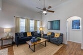 Located at 29980 FM-2978 in Magnolia, Texas, this two-story home offers a thoughtfully designed layout across two floors. The living room commands attention with soaring ceilings, crown molding, rich hardwood flooring, and an abundance of natural light streaming through large windows dressed with floor-length drapes and plantation shutters. A ceiling fan adds both function and style to the spacious room. The adjacent dining area features track lighting, a large natural wood dining table, and a striking geometric mirror wall accent. The kitchen is well-equipped with dark espresso cabinetry, granite countertop surfaces, stainless steel appliances, a center island with sink, and pendant lighting — all finished with warm wood flooring. The primary bathroom includes a dual-sink vanity with granite counters, dark cabinetry, a soaking tub, a separate shower, and a well-lit mirror. Secondary bathrooms echo the same refined finishes with granite vanities and wood-style flooring. Bedrooms are bright and inviting, with one featuring a charming window seat with built-in storage and another showcasing bold, colorful décor with crown molding details. Throughout the home, consistent crown molding, neutral tones, and quality finishes create a cohesive and welcoming atmosphere.